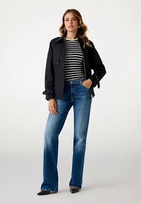Black jacket with rolled sleeves over a striped long-sleeve top, paired with light blue flared jeans and black pointed shoes.
