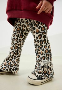 Gekürzte Cord-Hosen mit beigem Grundton und schwarz-braunen Leopardenflecken. Mit einem Minnie-Mouse-Patch und fransigem Saum. Getragen mit schwarzen Turnschuhen.