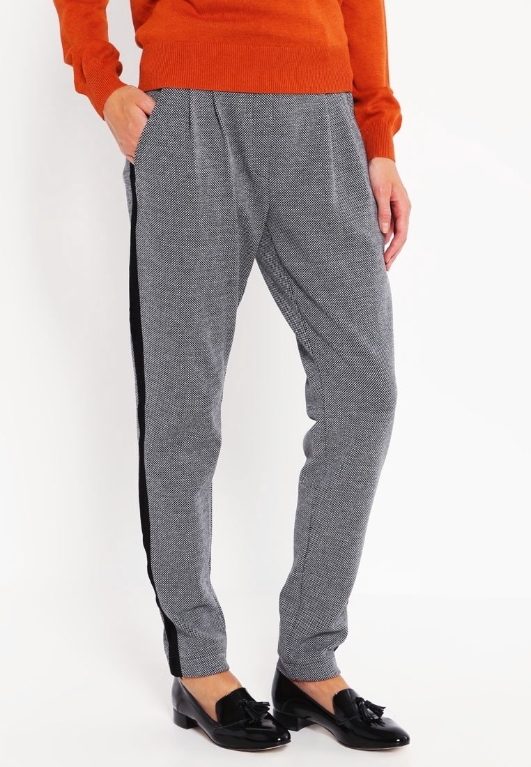 Pantalons à motif pied-de-poule gris avec des rayures noires sur les côtés, coupe fuselée, poches avant et taille élastique ; associés à des chaussures plates noires.