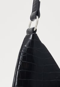 Svart krokodilmönstrad läderväska med texturerad yta, utrustad med en silverfärgad metallring på en platt rem.