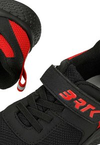 Scarpe da ginnastica nere con dettagli rossi, materiale a rete, suola nera texturizzata e cinturino in velcro. Presentano lacci e una linguetta posteriore per una facile calzata.
