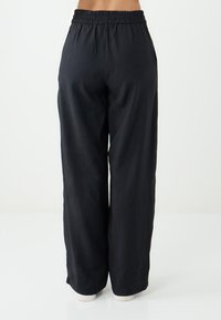 Schwarze weit geschnittene Hose mit elastischem Bund, die eine glatte Textur aufweist und keine sichtbaren Muster oder Hardware-Details hat.