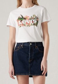 Weißes Baumwoll-T-Shirt mit einem bunten floralen und Kolibri-Graphic sowie dem Text "Levi's", kombiniert mit einem dunklen Denim-Minirock.