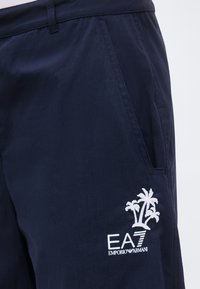 Σκούρο μπλε σορτς με λοξή πλαϊνή τσέπη και λευκό λογότυπο EA7 Emporio Armani με κέντημα φοίνικα στον μηρό.