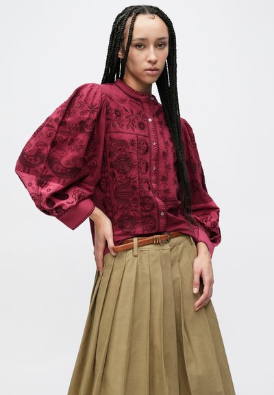 Vīna sarkanas izšūtas blūzes ar uzpūstām piedurknēm un pogu aizdari, kombinētas ar krokotu haki svārku un brūnu jostu. Detalizēts ziedu raksts.