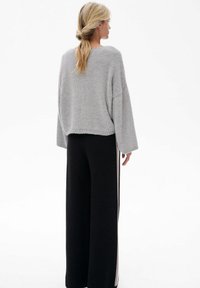 Jasnoszary, oversize sweter o luźnym kroju i teksturowanym wzorze, w zestawie z czarnymi spodniami w kant o wysokim stanie i szerokich nogawkach, z bocznymi paskami.