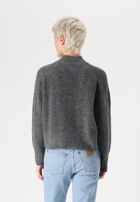 Gray ribbed knit sweater with a high neckline and dropped shoulders, paired with light blue denim jeans featuring a leather patch on the back.