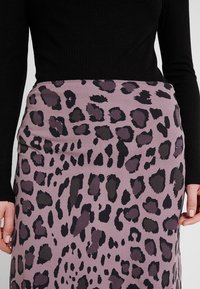 Lepardmönstrad kjol i ljuslila med mörka fläckar; slät textur, figursydd design, midilängd, ihopparad med en svart ribbad långärmad topp.