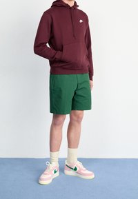 Vínová mikina s kapucí a přední kapsou s logem, zelené šortky, podkolenky a růžové tenisky se zelenými detaily. Jednoduchá textura, ležérní design.