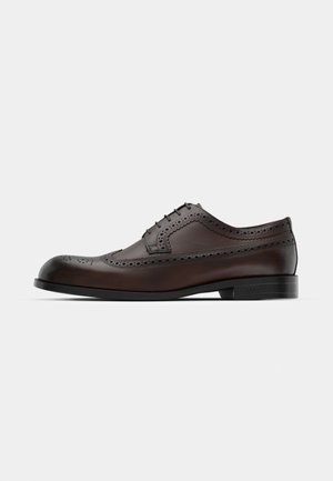 Chaussure habillée en cuir marron avec des détails de brogue, fermeture à lacets, bout arrondi et semelle plate. Présente des surfaces lisses et texturées.