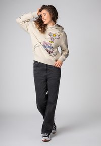 Crème hoodie met speelse grafische ontwerpen in roze, geel en zwart. Gecombineerd met hoge zwarte jeans en zwartwitte sneakers.