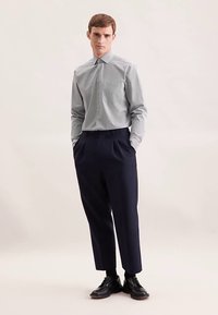 Jasnoszara koszula zapinana na guziki z subtelnym wzorem, zestawiona z granatowymi, wysokim stanem spodniami i czarnymi eleganckimi butami. Gładka tkanina i dopasowany krój.