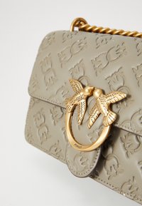 Beige geprägte Lederhandtasche mit einem goldfarbenen Vogelverschluss. Verfügt über eine strukturierte Oberfläche und einen Ketten-Schultergurt.