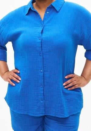 Chemise bleu à manches courtes avec un tissu texturé et léger, offrant une coupe décontractée. Associée à un pantalon bleu assorti.