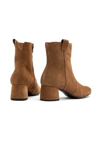 Brązowe zamszowe botki za kostkę z zaokrąglonym noskiem, średniej wysokości słupkowym obcasem i zamkiem błyskawicznym z boku. Posiadają pętelkę z tyłu ułatwiającą zakładanie.