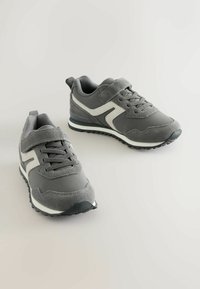 Gray sports shoes with a combination of textured fabric and smooth suede, featuring white accents, laces, and a Velcro strap for closure.