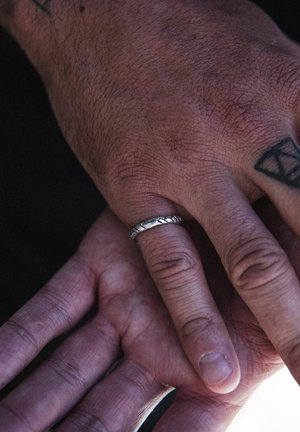 Ezüst gyűrű csavart mintával egy ujjon; két kéz finoman érintkezik, bemutatva a bőr textúráját és a különböző bőrszíneket.
