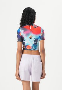 Top pendek lengan pendek yang dipotong, menampilkan desain grafis multicolor dengan elemen olahraga. Dip搭ou dengan celana pendek lavender muda yang dilengkapi kantong.