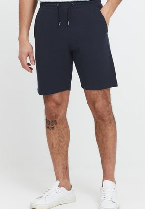 Navy blue cotton shorts with an elastic waistband, drawstring, and two side pockets; ends just above the knee. White sneakers.