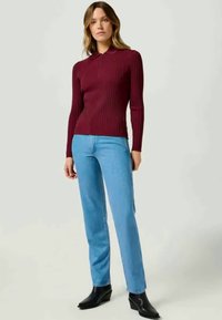 Burgundia ribadeeritud pika varrukaga pluus, millele on sobitatud helesinised sirged teksad ja mustad pahkluu saapad. Siledast kangast ja kraega kaelus.