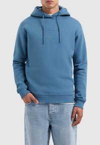 Blauwe sweatshirt met capuchon, voorste kenguruzak, ribgebreide manchetten en zoom. Voorzien van trekkoorden en minimale branding op de borst.