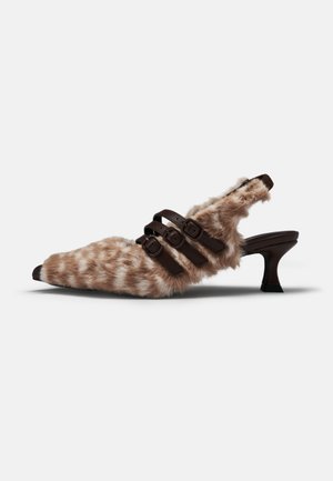 Chaussure slingback à bout pointu en fourrure avec trois brides à boucle marron foncé et un talon bas courbé sur fond blanc.