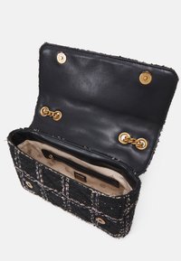 Sort tweed håndtaske med guld kæde detaljer, beige mønstret indvendig foring, lynlåslomme og magnetisk lukning, åben og tom.