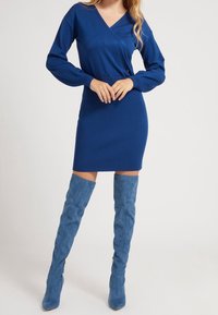 Robe bleu côtelé avec un décolleté en V et des manches longues, associée à des bottes bleues au-dessus du genou. La robe présente une silhouette ajustée et des accents subtils.