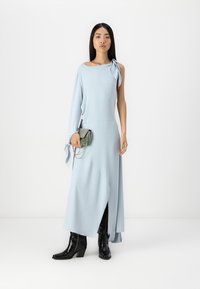 Ανοιχτό μπλε ασύμμετρο φόρεμα με δεσίματα στον αριστερό ώμο και πλαϊνό σκίσιμο. Φορεμένο με μαύρες γόβες μέχρι τον αστράγαλο και μεταλλική τσάντα-χιαστί.