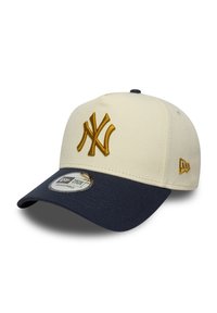 Cremefarbener Hut mit einer marineblauen Krempe, ausgestattet mit einem bestickten goldenen "NY"-Logo und einem New Era-Aufkleber. Verstellbarer Riemen auf der Rückseite.