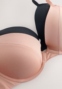 Zwei gepolsterte BHs in Schwarz und Beige, nebeneinander auf einer hellen Oberfläche mit sichtbaren Trägern gezeigt.