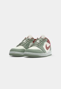 Une paire de baskets basses avec des panneaux blancs, vert pâle et rouge pâle, des lacets gris et un swoosh rouge de Nike sur un fond blanc.