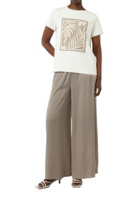 Light green T-shirt with a beige abstract leaf print, paired with beige wide-leg pants and strappy white heels. Smooth fabric texture.