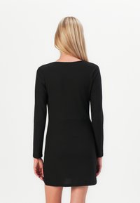 Svart langermet kjole med rund hals, figursydd design, mid-thigh lengde, glatt tekstur og subtile sidesplitter ved kanten.