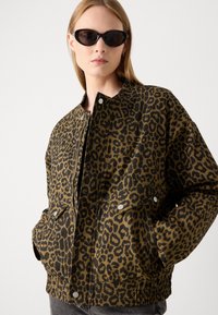 Jakke med leopardmønster i brune og svarte farger, laget av teksturert stoff, med trykknapper og avslappet passform.