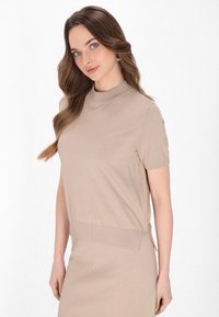 Beige striktop med korte ærmer, ribbet halsudskæring og kant. Glat tekstur med en subtil glans. Parret med en matchende nederdel.
