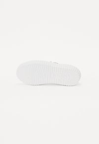 Hvid sneakersål med dybe riller og et mønstret tekstur, der har mærkenavnet "Reebok" præget på den ydre kant.