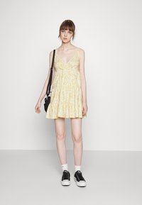 Vestido floral amarelo com decote em V, al�ças finas e saia em camadas. Estilizado com ténis pretos e meias brancas para um look casual.