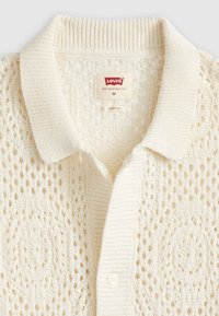 Crème-kleurige gebreide cardigan met opengewerkte patronen, geribde kraag, één knop en Levi's maat M label binnenin de hals.