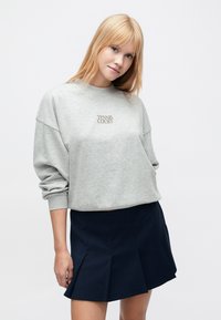 Γκρι φούτερ με κεντημένο το "TENNIS COURT" σε χρυσό. Χαλαρή εφαρμογή με χαμηλωμένους ώμους, συνδυασμένο με σκούρα πλισέ φούστα.