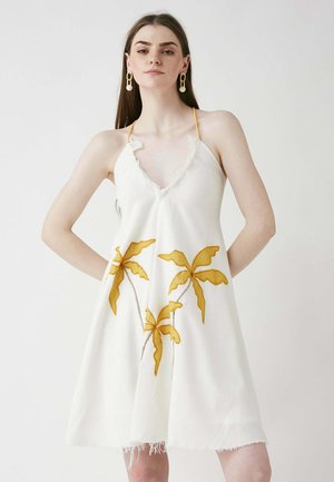 Weißes ärmelloses Kleid mit tiefem V-Ausschnitt, verziert mit gelben gestickten Palmenblättern und fransigem Saum. Dünne Schulterträger runden das Design ab.