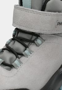 Botte de randonnée gris clair avec lacets élastiques noirs, accents bleu clair et large bride à boucle auto-agrippante à la cheville.