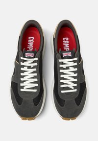 Sneakers in suede e rete grigio con lacci bianchi, dotati di una soletta rossa e un accento beige. La suola presenta un motivo di battistrada marrone.
