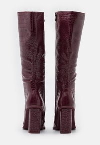 Stivali al ginocchio bordeaux con texture a coccodrillo, tacco quadrato e chiusura con zip sul retro. Finitura liscia e design strutturato.