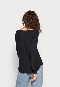 Černá dlouhá košile s volným výstřihem na rameni, vyrobená z měkké tkaniny, spárovaná s modrými džínami s vysokým pasem.