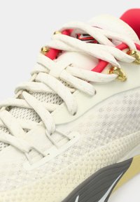 Hvid sneakers med mesh og glat lædermaterialer. Har rosa accenter, guld øjer og en struktureret grå sål. Snørebånd og logo synlige.