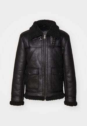 Schwarze Lederjacke mit einem flauschigen Kragen, Reißverschluss und zwei Fronttaschen. Merkmale dekorativer Beschläge und Details in der Naht.