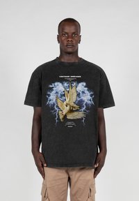Svart bomullsgrafisk t-skjorte med et sentralt bilde av to duer mot en stormfull blå bakgrunn med lyn, merket "VINTAGE DREAMS."