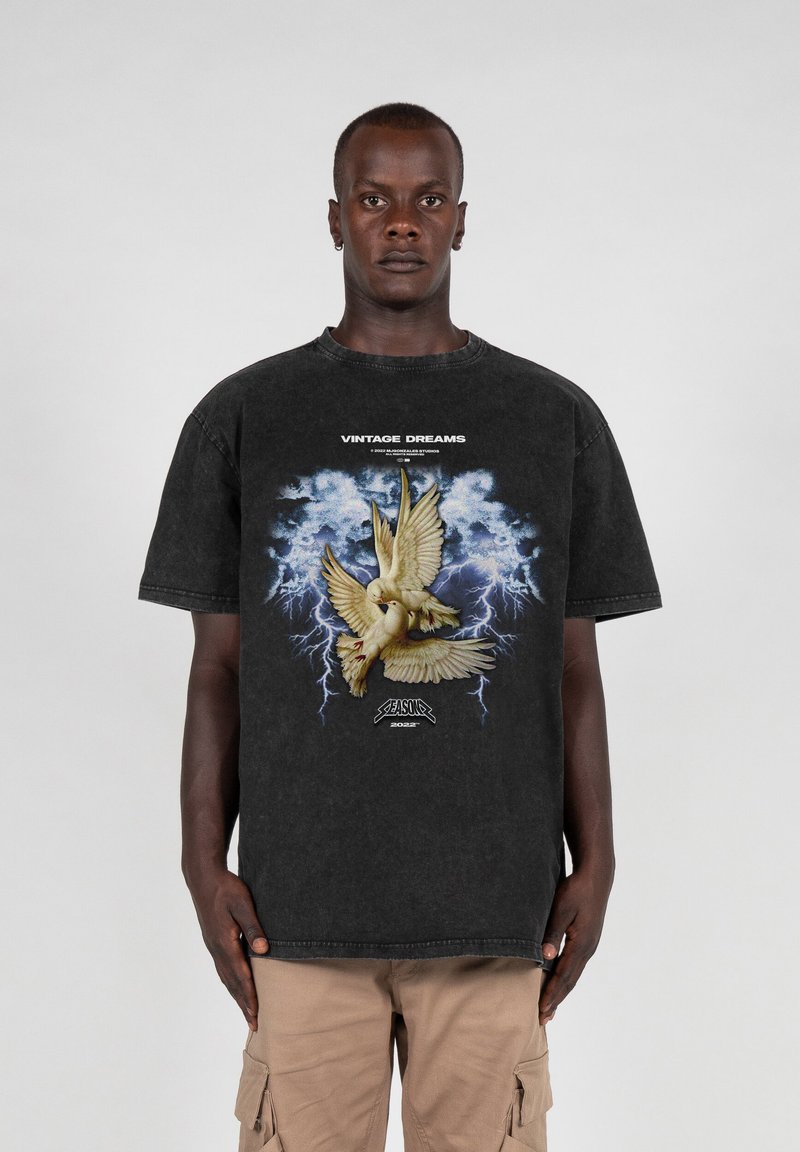 Camisa gráfica de algodón negra con una imagen central de dos palomas sobre un fondo azul tormentoso con relámpagos, etiquetada como "SUEÑOS VINTAGE".