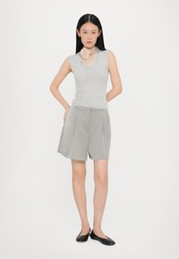 Top senza maniche grigio chiaro con scollo a V, abbinato a pantaloni corti grigi larghi. Scarpe nere flat completano il look. Accessorio per il collo intricate.